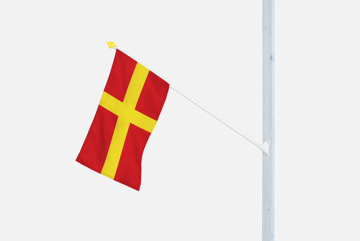 Skånsk fasadflagga set som sitter uppskruvad med ett plast fäste på en fasad med vit bakgrund