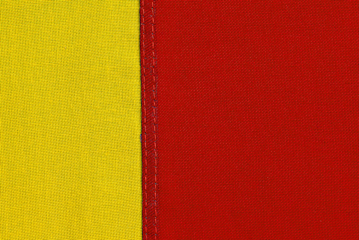 Närbild på en skånsk flagga där man ser textilens struktur, sömmen och tråden.