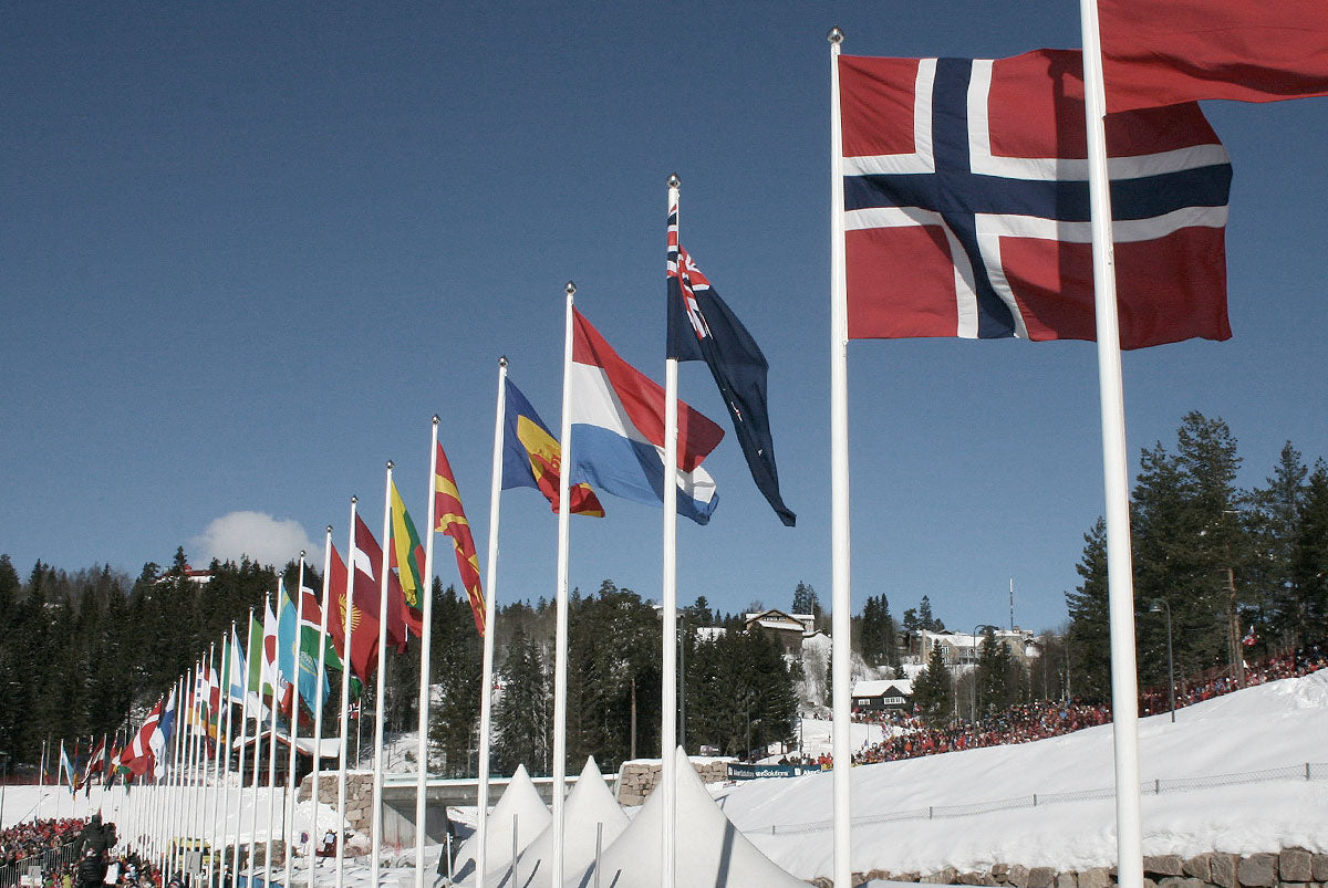 Nationalflaggor upphissade i flaggstänger i flera olika länder sitter uppradade  utomhus i Oslo med en blå himmel som bakgrund