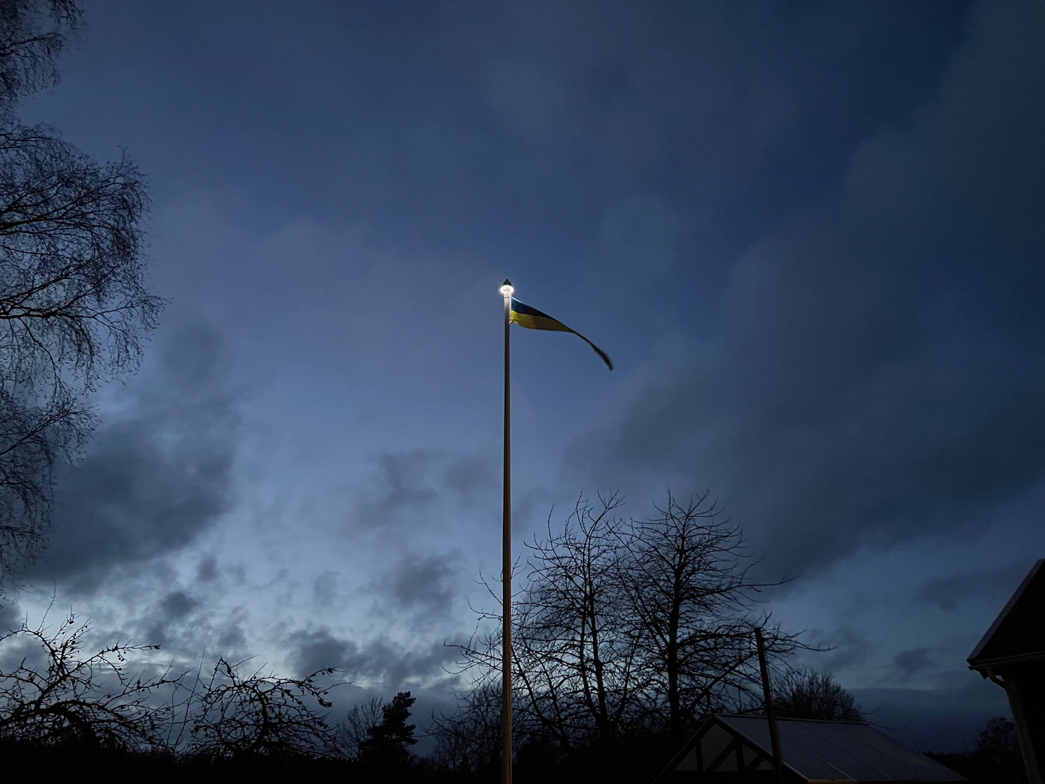 Solcellsdriven flaggstångs belysningen lyser upp en flagga och en flaggstång i mörkret 
